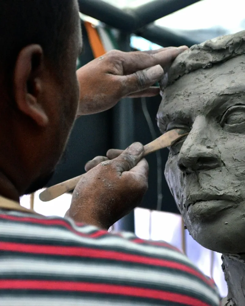 Manos modelando con palillo la zona del ojo en un retrato de barro